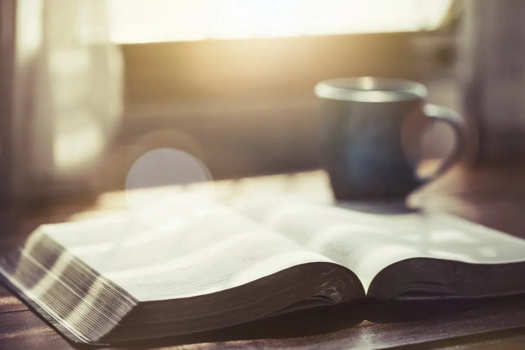close up of open bible with a cup of coffee for morning devotion on wooden table with window light