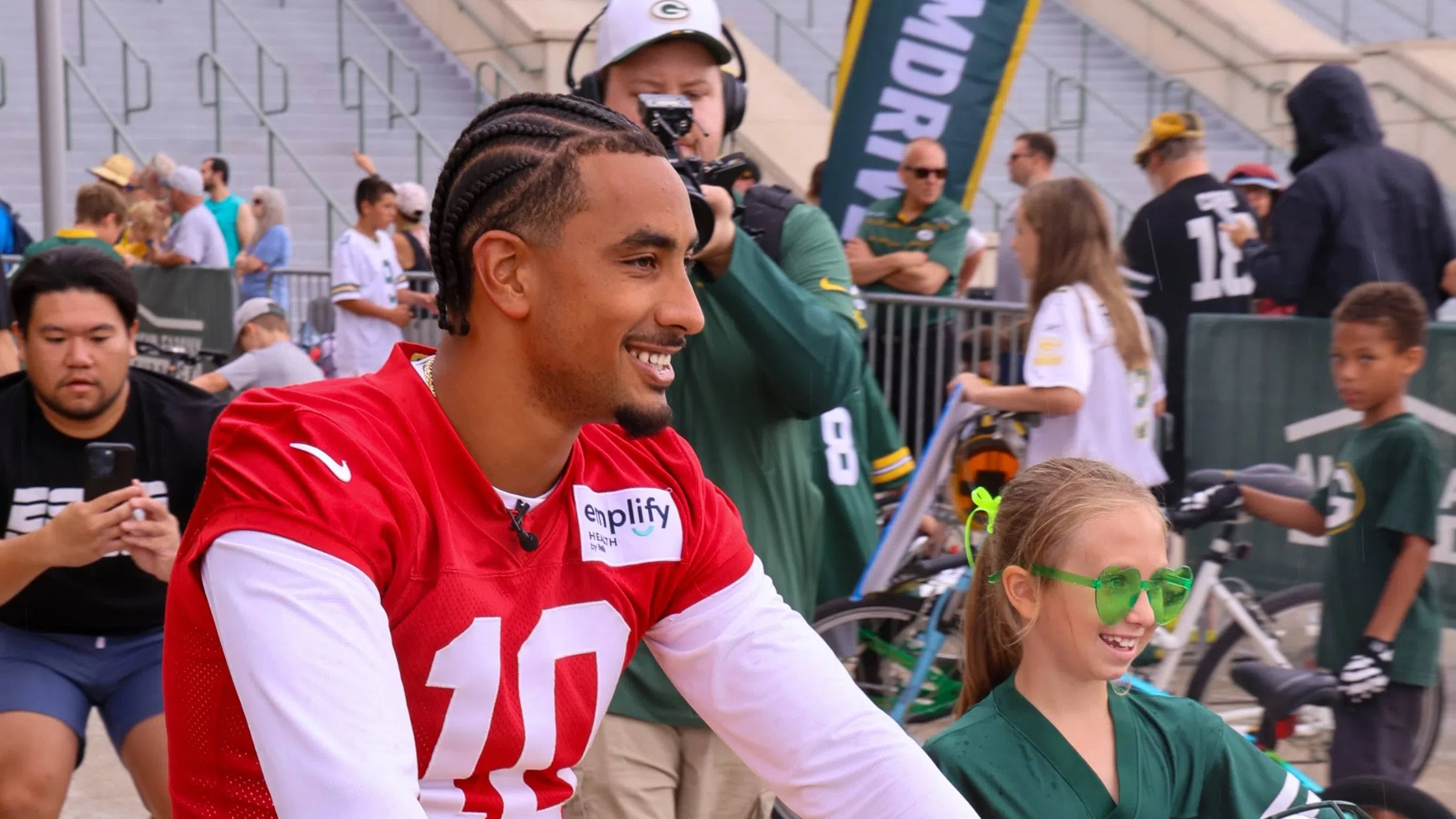 Picture of Jordan Love at 2025 Green Bay Packers Training Camp riding a bicycle with a child walking beside.