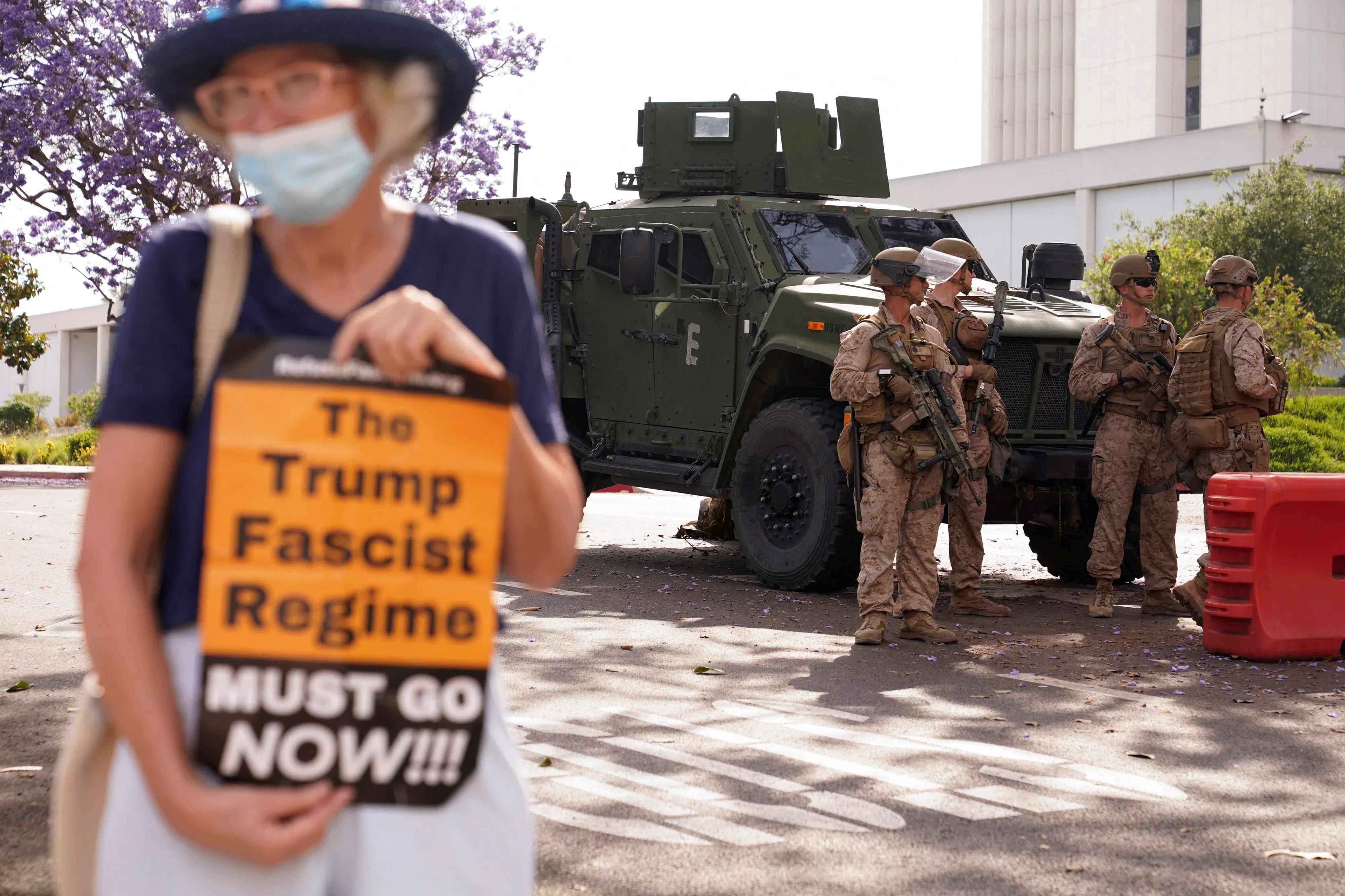 A woman holds a pamphlet as U.S. Marines stand guard outside the Wilshire Federal Building, after they were deployed to Los Angeles as federal immigration sweeps continue, in Los Angeles, California, U.S., June 13, 2025. REUTERS/David Ryder