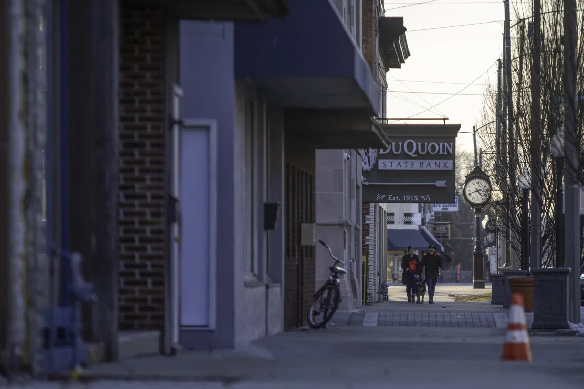 Two people walk a dog on the sidewalk