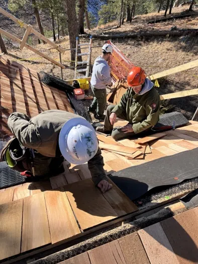 Three people in uniform and safety equipment doing work on top of a roof