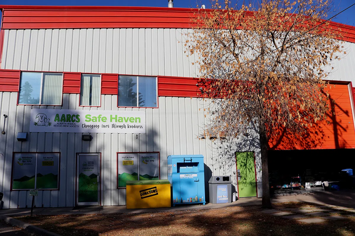 The exterior of the AARCS shows the main entrance and signage for the Alberta Animal Rescue Crew Society, including information for the onsite veterinary clinic, along with donation bins outside.