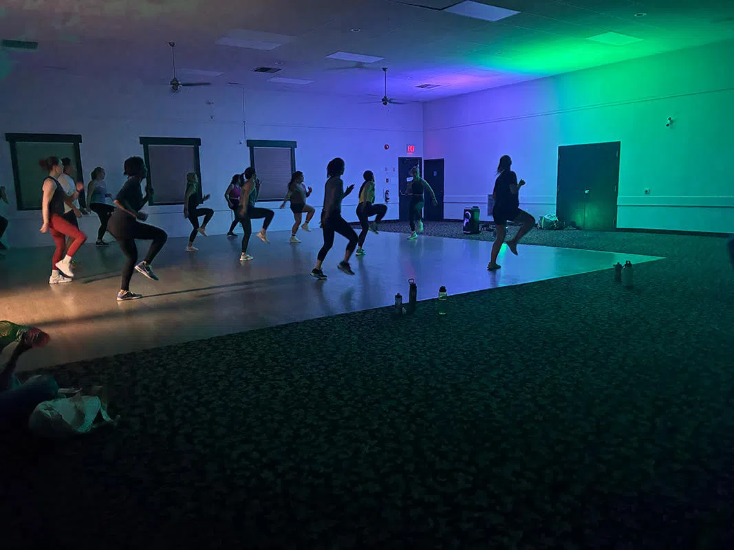 Multiple people participating in high fitness and dancing with coloured lights in the background.