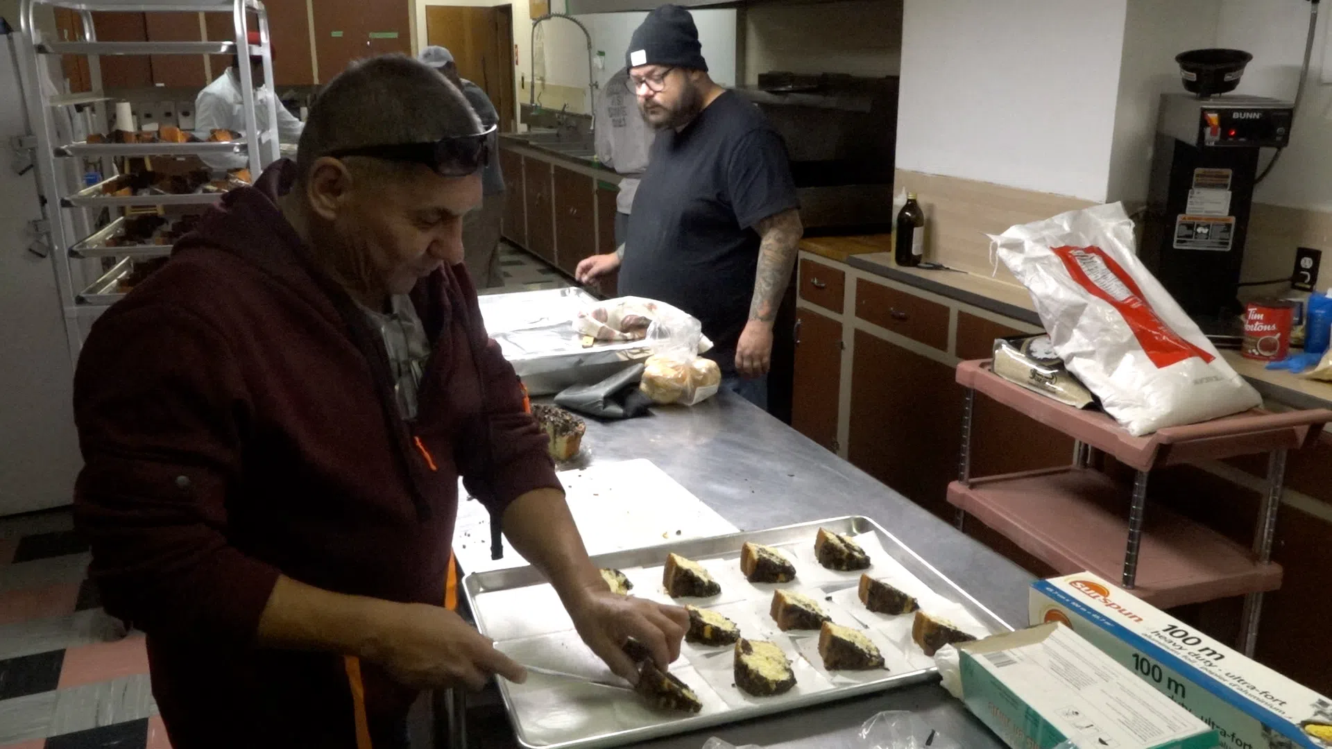 A busy kitchen environment. A cook places cut pastries onto a pan.
