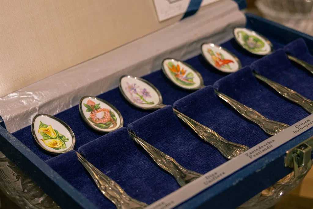 Ornate spoons with flowers painted on them. They're in a blue velvet case. There are labels for the flowers at the base of it.