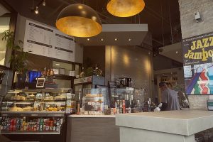 A landscape image of the interior of Kawa Espressp Bar, featuring its bakery display, menu, overhead lighting, and service counter.