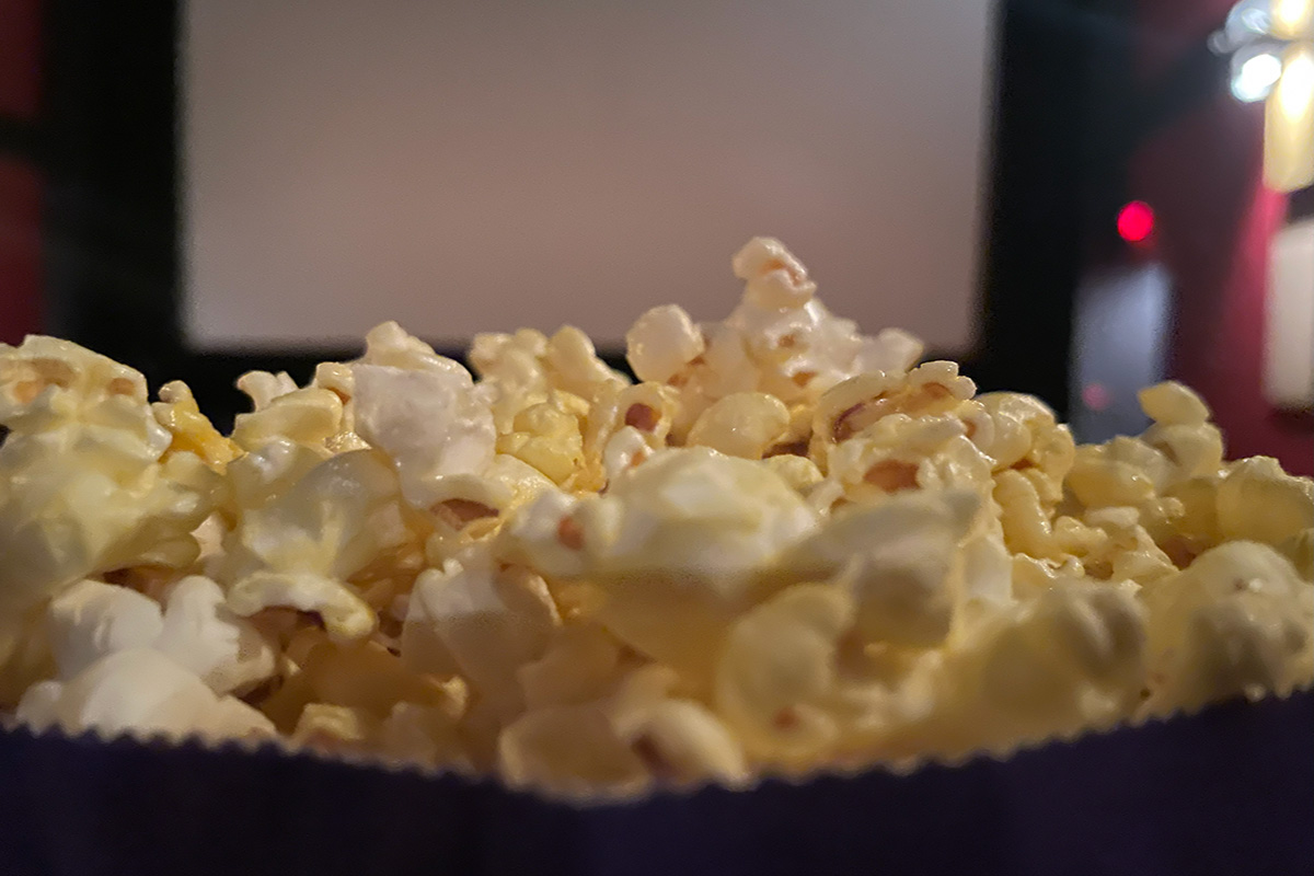A close up of buttery popcorn in a movie theatre room in Canyon Meadows Cinemas. The popcorn is towards the bottom of the frame and shines in the light. The main light comes from the right hand side of the frame.