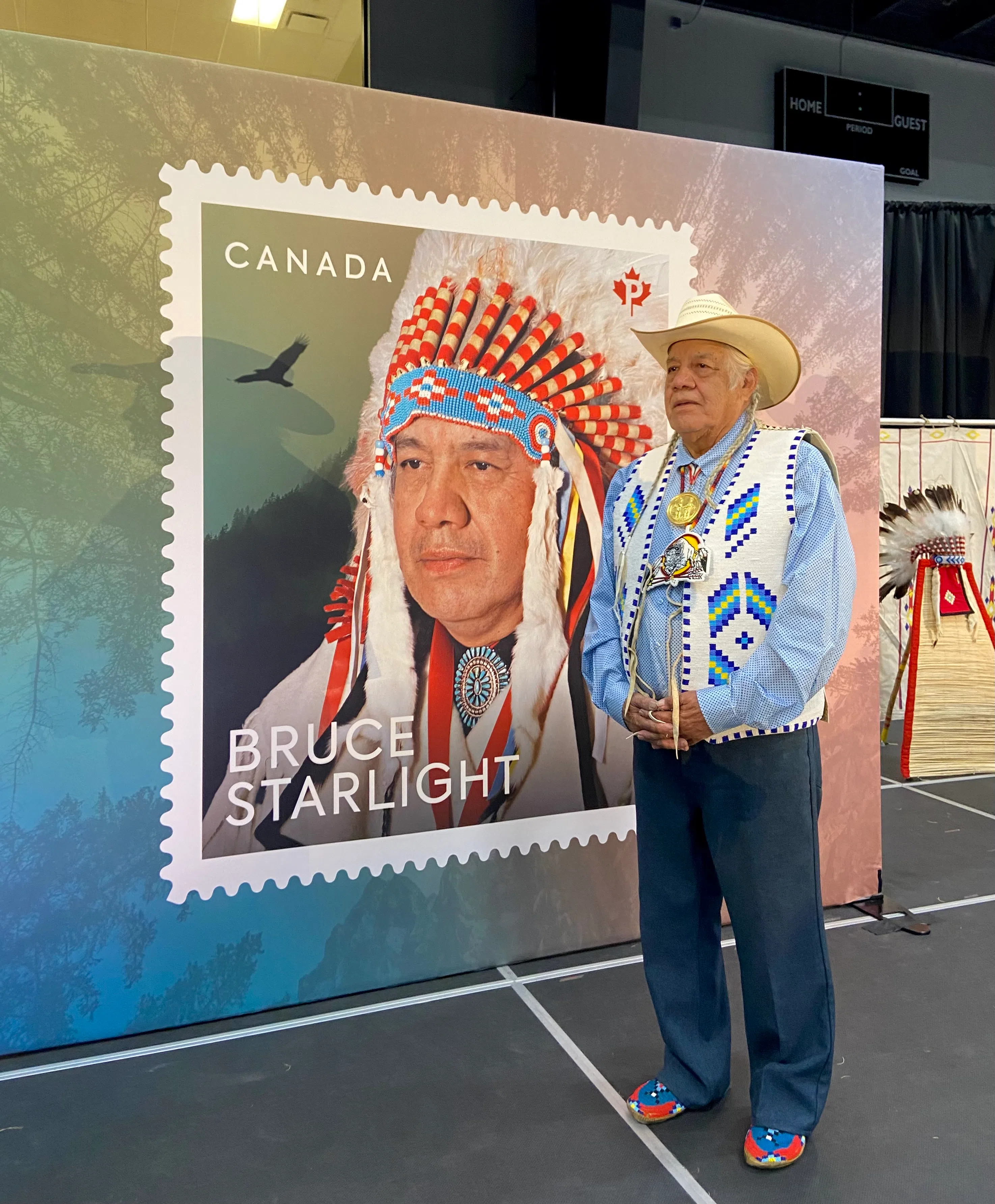 Bruce Starlight in front of the Canada Post stamp made in his honor for his work in preserving the Tsúut'ínà language. Photo at the unveiling by William L Baliko