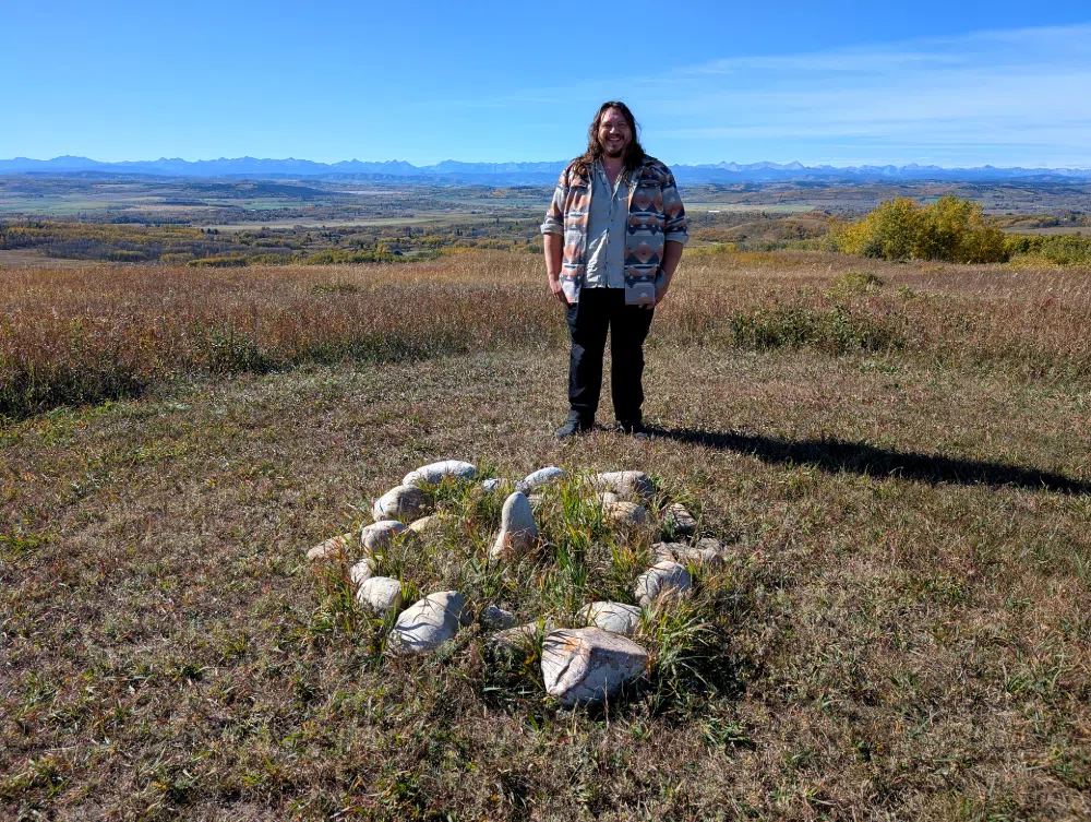 Jared Tailfeathers stand behind one of his art pieces