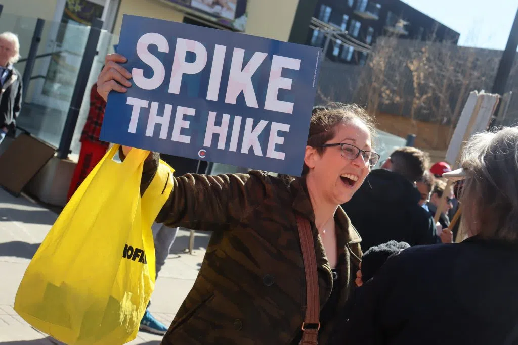Protester holding a sign that reads "Axe The Hike" on 124 Street near Jasper Ave (Photo Credits - Daniel Barker-Tremblay)