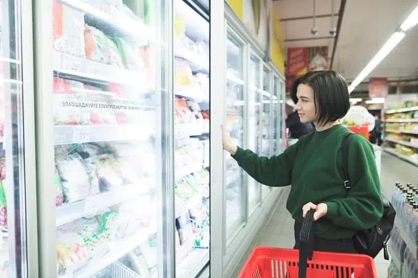 The buyer near the refrigerator in the supermarket. A beautiful girl buys food at a supermarket. The buyer selects the goods in the store