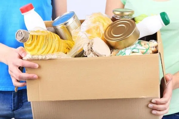 Volunteers with donation box with foodstuffs on grey background