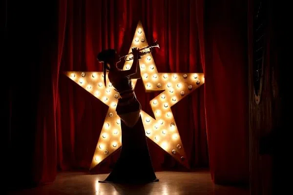Woman on stage play on the trumpet.Red velvet curtain with Brodway star on background