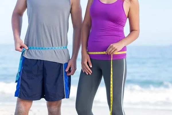 Couple measuring their waist at the beach