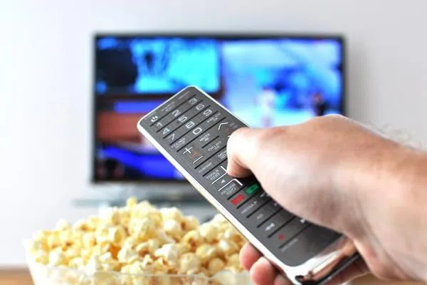 Remote control in the hand against pop-corn and TV-set