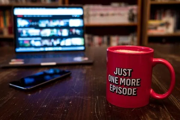 Watching series with a cup of tea on wood table with cellphone. Just one more episode. Millennial concept