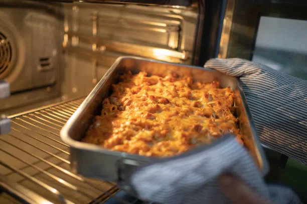 woman hands taking baked homemade macaroni with cheese with a crispy top out of the oven - mac and cheese oven stock pictures, royalty-free photos & images