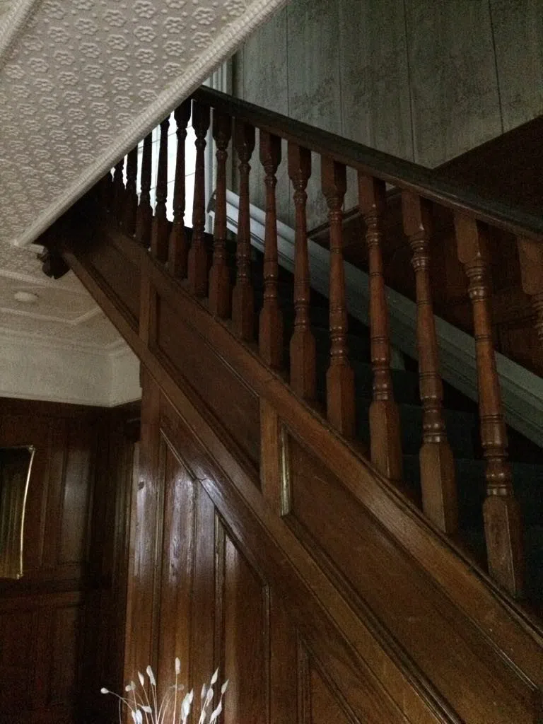 Close-up of McDonald House staircase with wooden paneling and pressed-tin ceiling