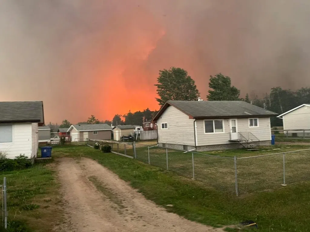 Flames and smoke rise behind houses in Beauval during wildfire threat