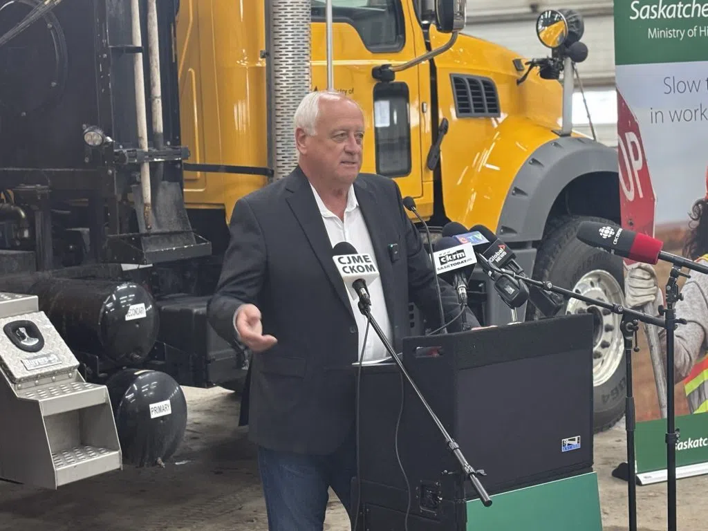 David Marit speaking at a podium with microphones in front of a Ministry of Highways truck during the Orange Zone Construction Update announcement