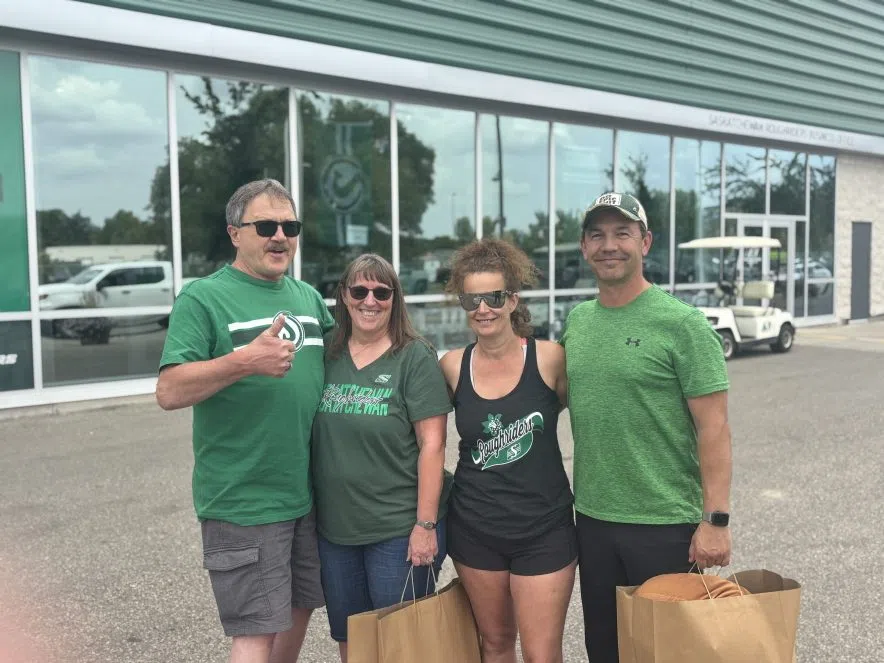 Saskatchewan Roughriders fan Chuck Anderson on the left wearing a green Riders shirt and giving a thumbs up, standing with three family members holding shopping bags outside Mosaic Stadium’s Rider Store.