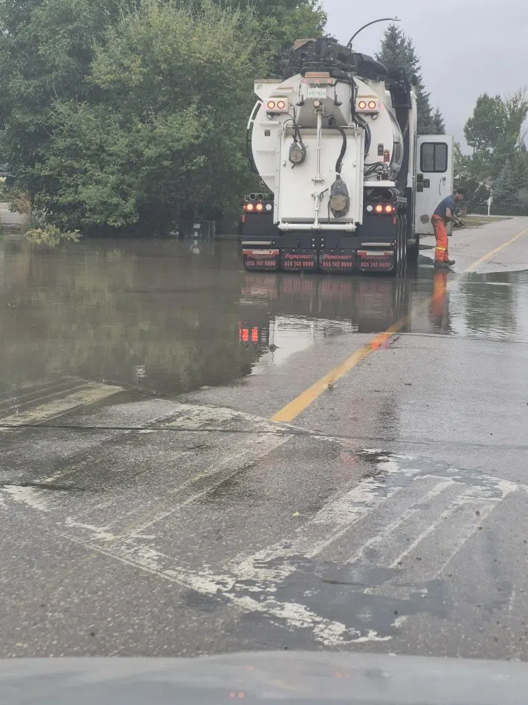 Vacuum truck with a large hose draining floodwater from a residential street while a worker monitors the process.