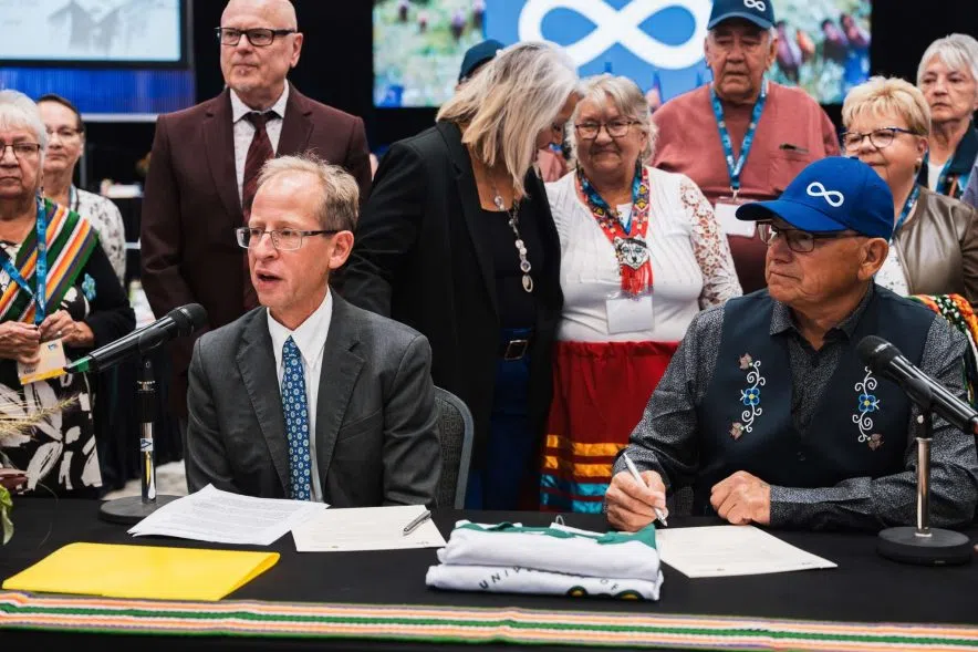 University of Regina president Jeff Keshen and Métis Nation–Saskatchewan president Glen McCallum sign the citizenship agreement at a table with delegates watching.