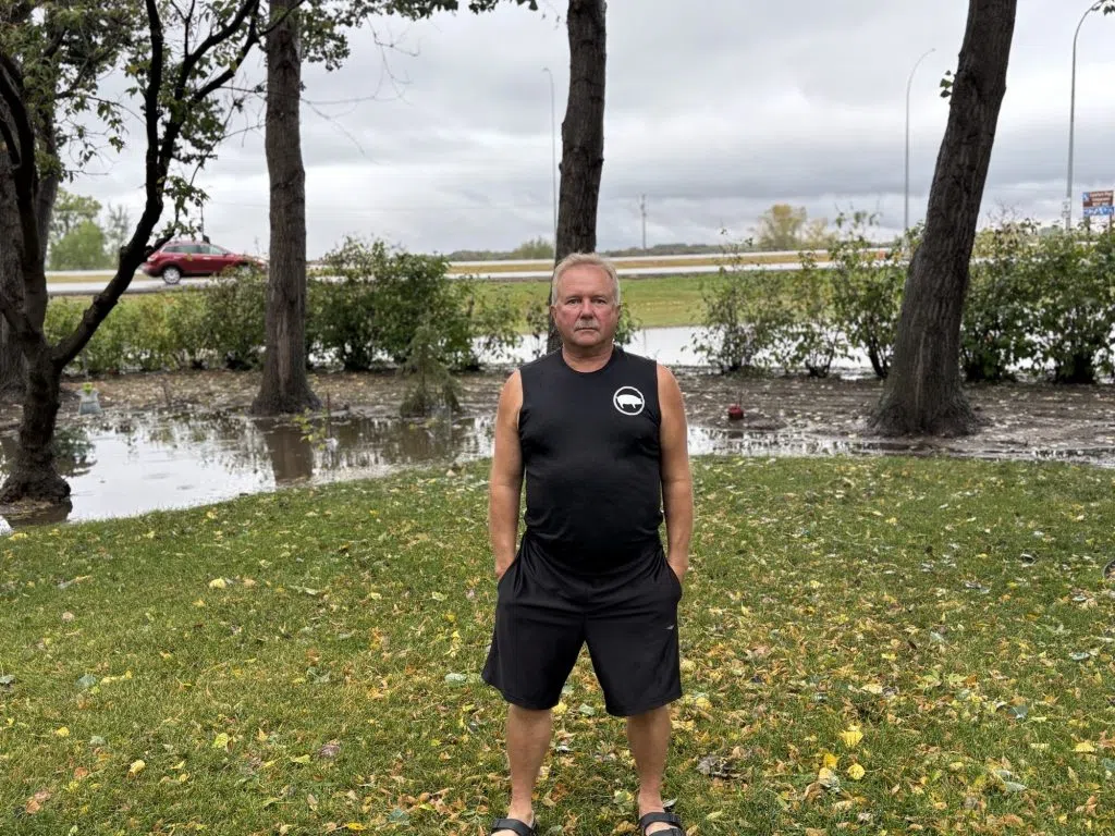 Man standing on grass in front of floodwater pooling in a residential yard after a rainstorm.