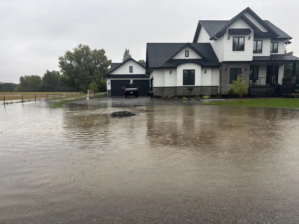 Two-storey house with water pooled across the driveway and yard during heavy rainfall.