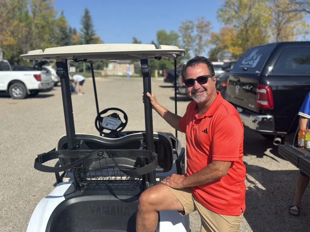 Pat Fiacco smiles beside a golf cart in the parking lot, enjoying one of the final sunny days of the season.