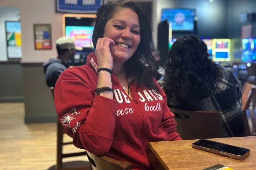 A woman wearing a red Blue Jays hoodie smiles at her table inside Boston Pizza in Regina during the playoff watch party.