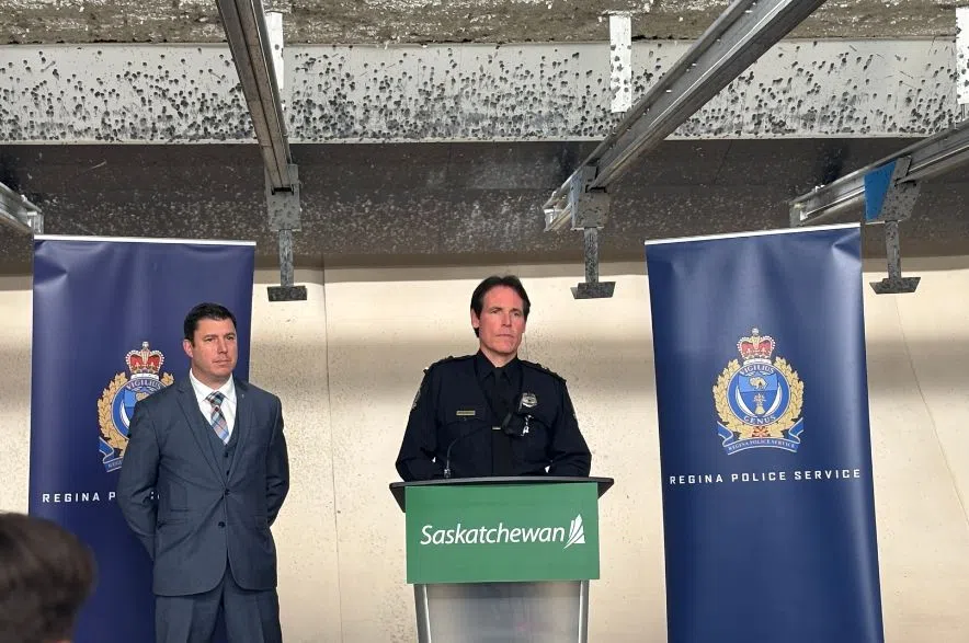 Regina Police Service Deputy Chief Trent Stevely speaks at a podium flanked by RPS banners, with MLA Michael Weger standing beside him during a funding announcement inside the police firearms range.