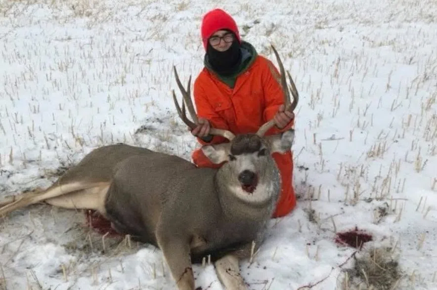 Zachary Schlageter kneels in snowy farmland holding a deer by its antlers after a successful hunt in southern Saskatchewan.