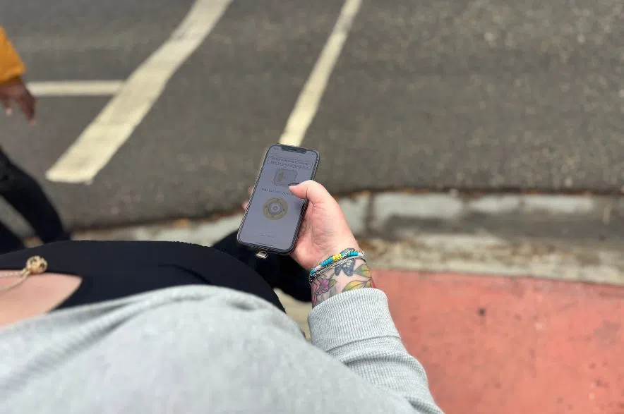 Close-up of a person holding a phone showing the PedApp screen while standing near a crosswalk curb on Victoria Avenue.