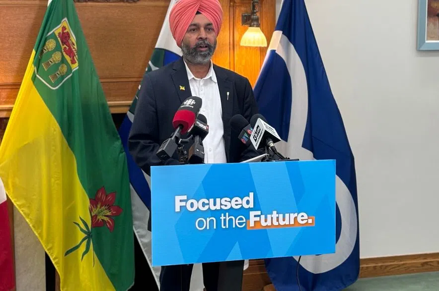 Tajinder Grewal speaks at a podium during a Saskatchewan NDP media availability at the Legislature, with Saskatchewan and Métis Nation flags displayed behind him.