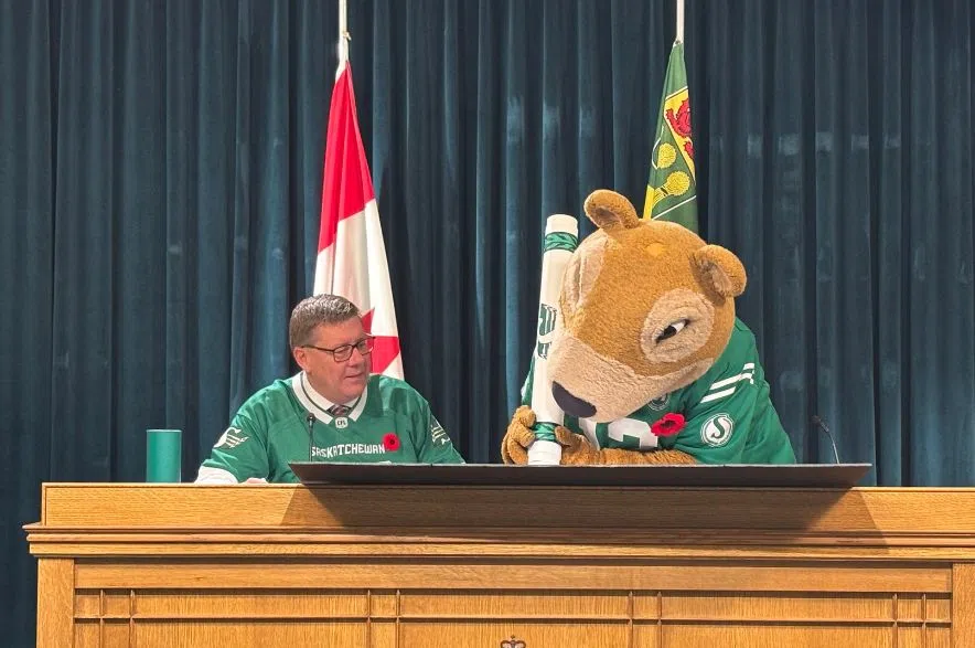 Gainer the Gopher signs the Green and White Day proclamation with a marker as Premier Scott Moe watches during the announcement.