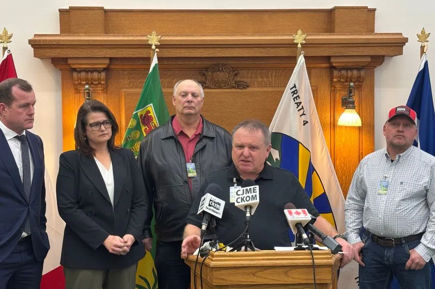 Quinton Jacksteit speaks at the podium inside the Legislative Building, with Trent Wotherspoon, Carla Beck, Kelly Bakanec, and Tyson Jacksteit standing behind him.