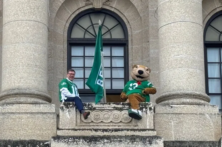 Premier Scott Moe and Roughriders mascot Gainer the Gopher wave a Riders flag from the Legislature balcony in Regina.