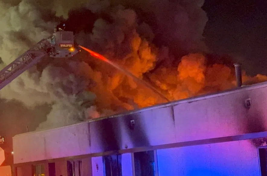Bright orange flames and thick black smoke billow from the roof of the Salvation Army building in Prince Albert while firefighters attack the blaze from an elevated ladder.