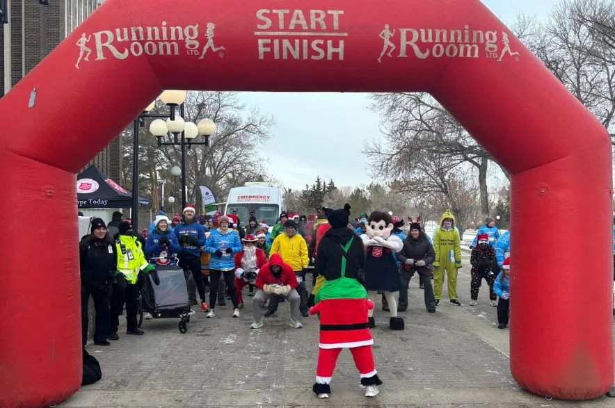 Crowd of runners in winter gear and holiday costumes line up under a red inflatable start-finish arch.
