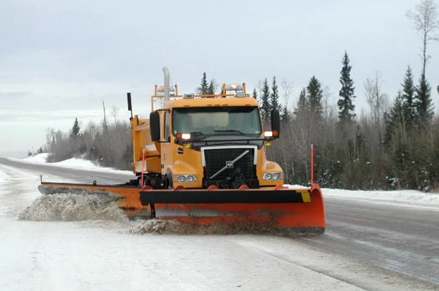 An orange plow clearing snow and ice from a Saskatchewan highway.