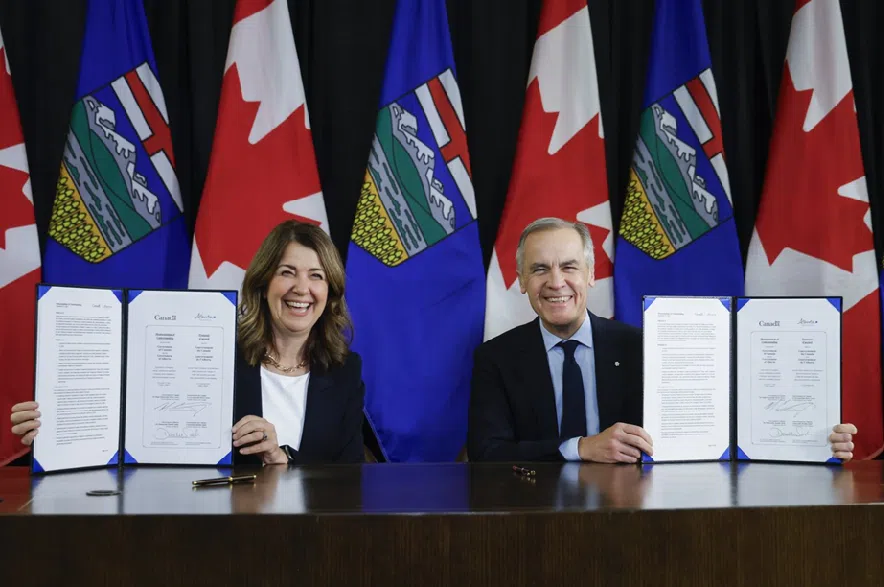 Prime Minister Mark Carney, right, signs a memorandum of understanding with Alberta Premier Danielle Smith in Calgary on Thursday, Nov. 27, 2025.