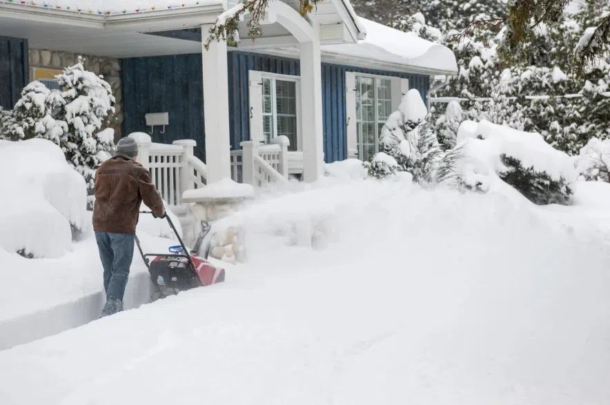 Man using snowblower to clear deep snow on driveway.