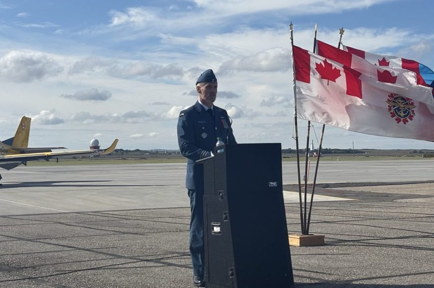 Lt.-Col. Craig Cloete speaks at a podium beside Canadian and military flags at 15 Wing Moose Jaw.