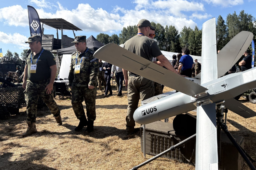 Military personnel walk past a drone.