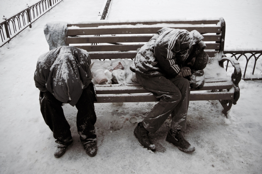 People sleeping on a bench in a park in winter.
