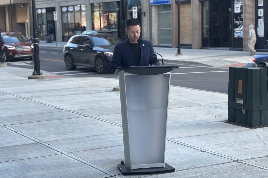 Regina Mayor Chad Bachynski addresses attendees from a podium along the newly reconstructed 11th Avenue in downtown Regina.