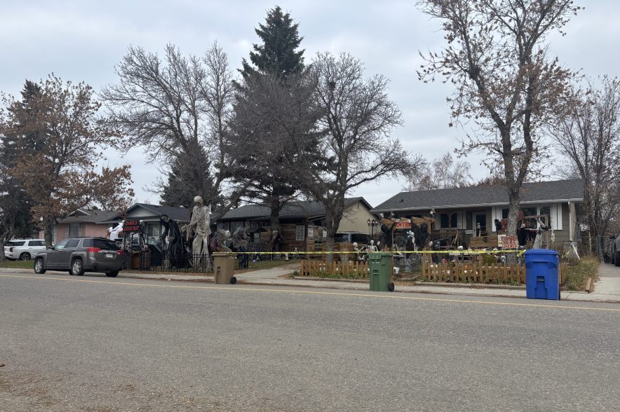 A Regina home features an elaborate Halloween display with towering skeletons, grim reapers, tombstones and other spooky decorations beneath a cloudy sky.
