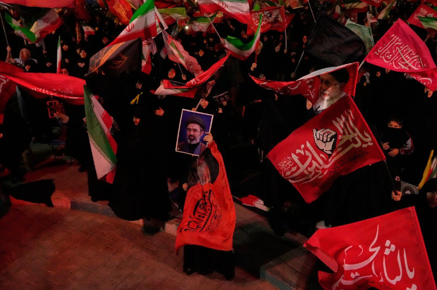 Demonstrators wave flags as one holds up a portrait of the Iranian Supreme Leader Ayatollah Mojtaba Khamenei.