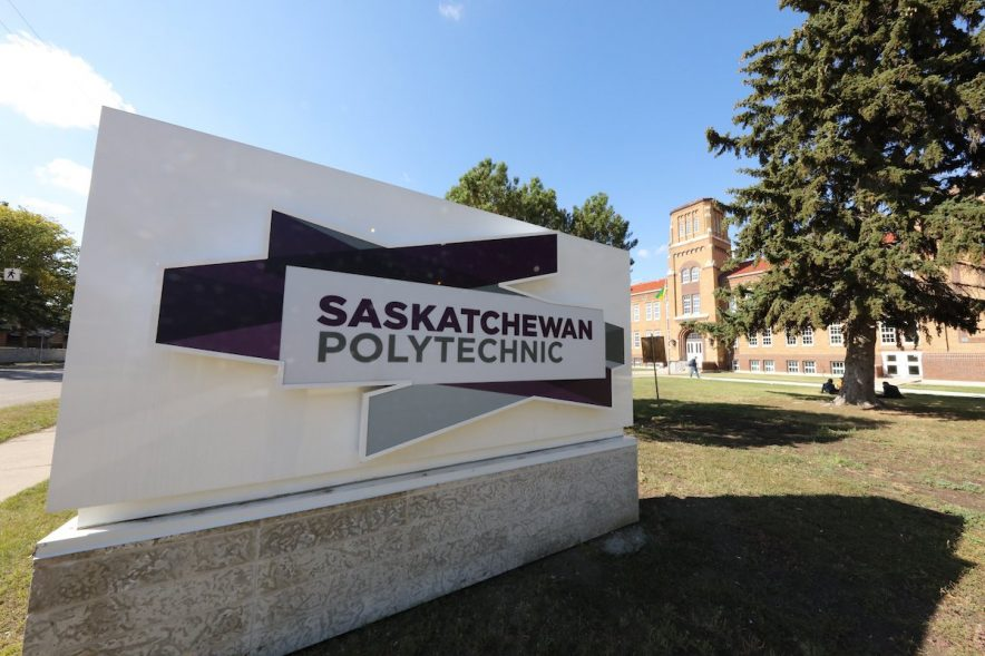 A white and purple sign in front of a Saskatchewan Polytechnic building.